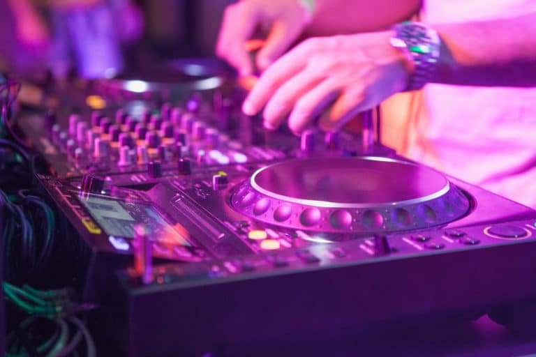 DJ playing music at mixer on colorful blurred background. The hands close up